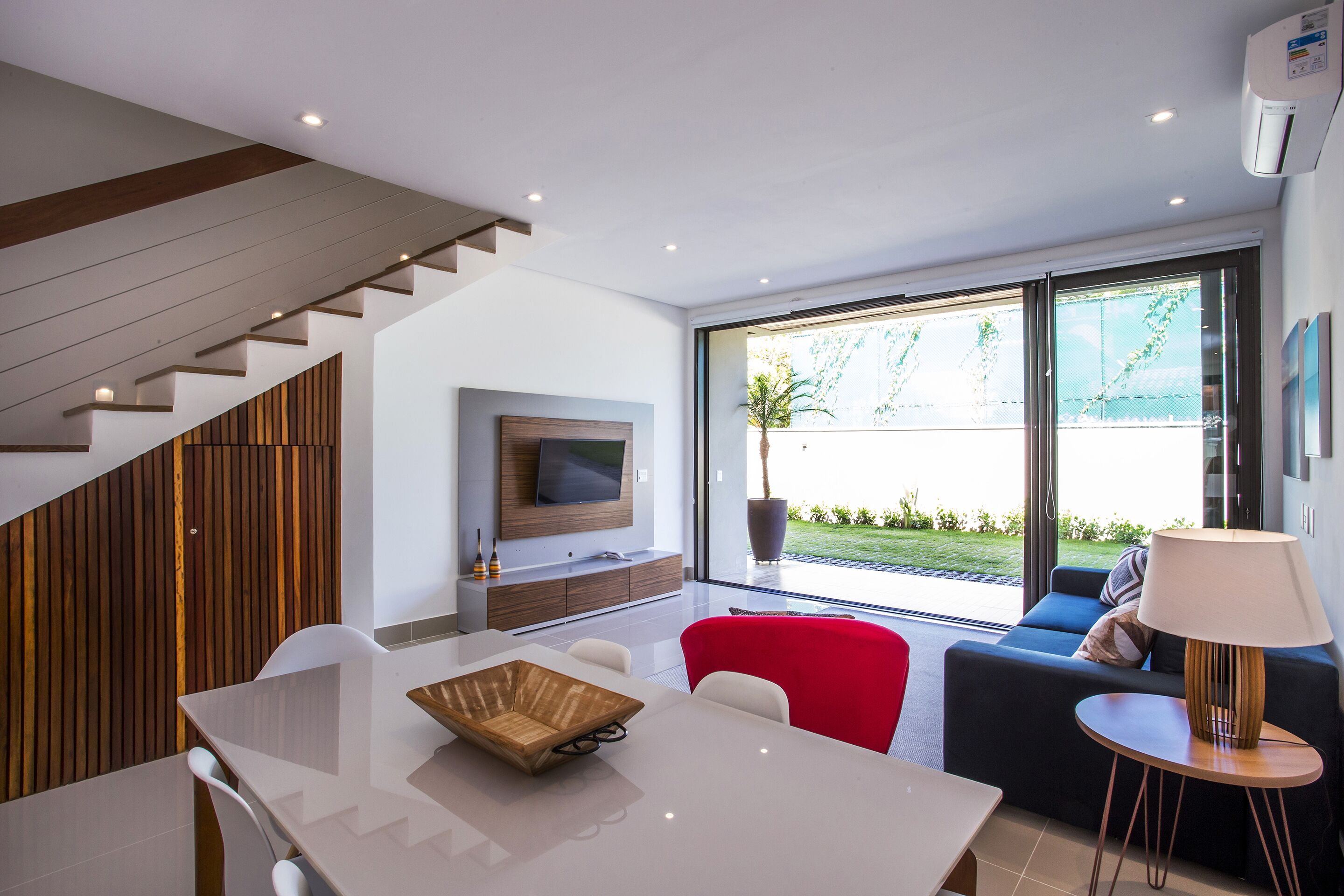 Een moderne woonkamer met een eethoek, een trap en een groot raam met uitzicht op de omgeving.