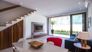 Een moderne woonkamer met een eethoek, een trap en een groot raam met uitzicht op de omgeving.