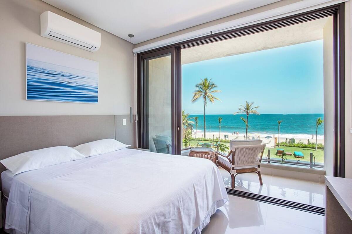 Une chambre d’hôtel avec un lit, une chaise et une vue sur la plage et l’océan.