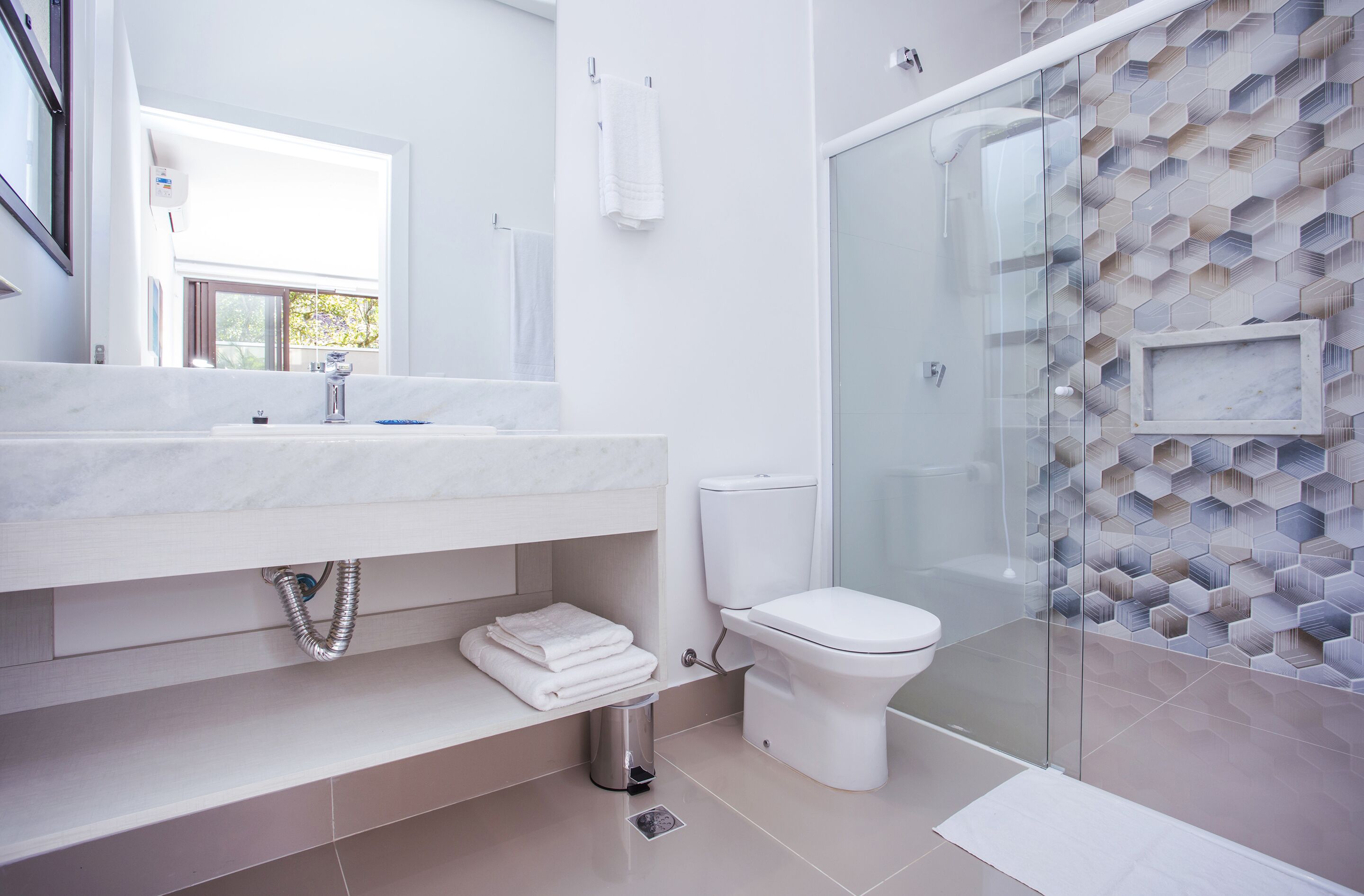 Een moderne badkamer met een marmeren wastafel, een toilet en een douchecabine met glazen wanden.