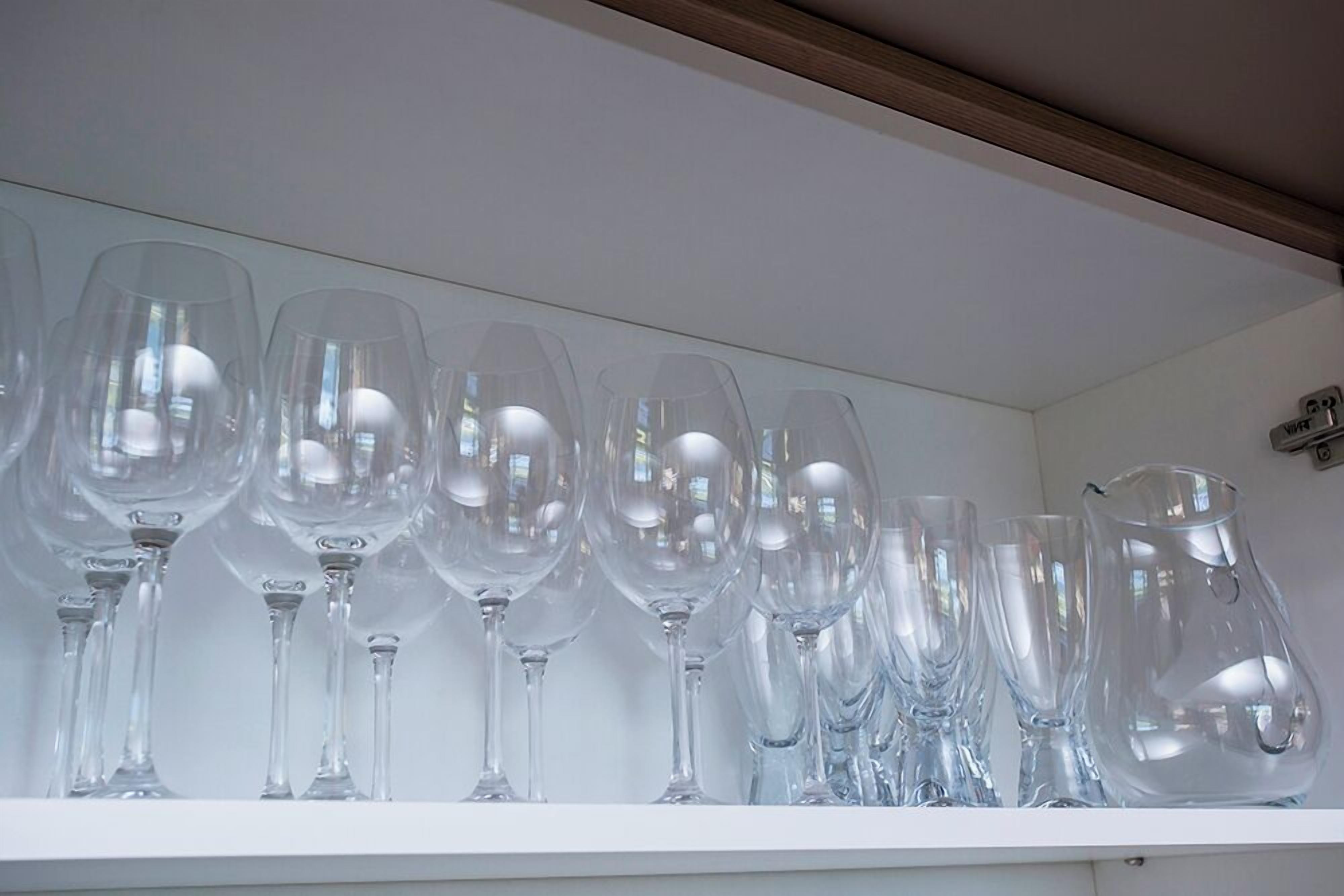 Uma prateleira branca com vários copos de vinho transparentes e um jarro de vidro.