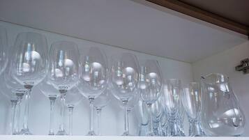 Uma prateleira branca com vários copos de vinho transparentes e um jarro de vidro.