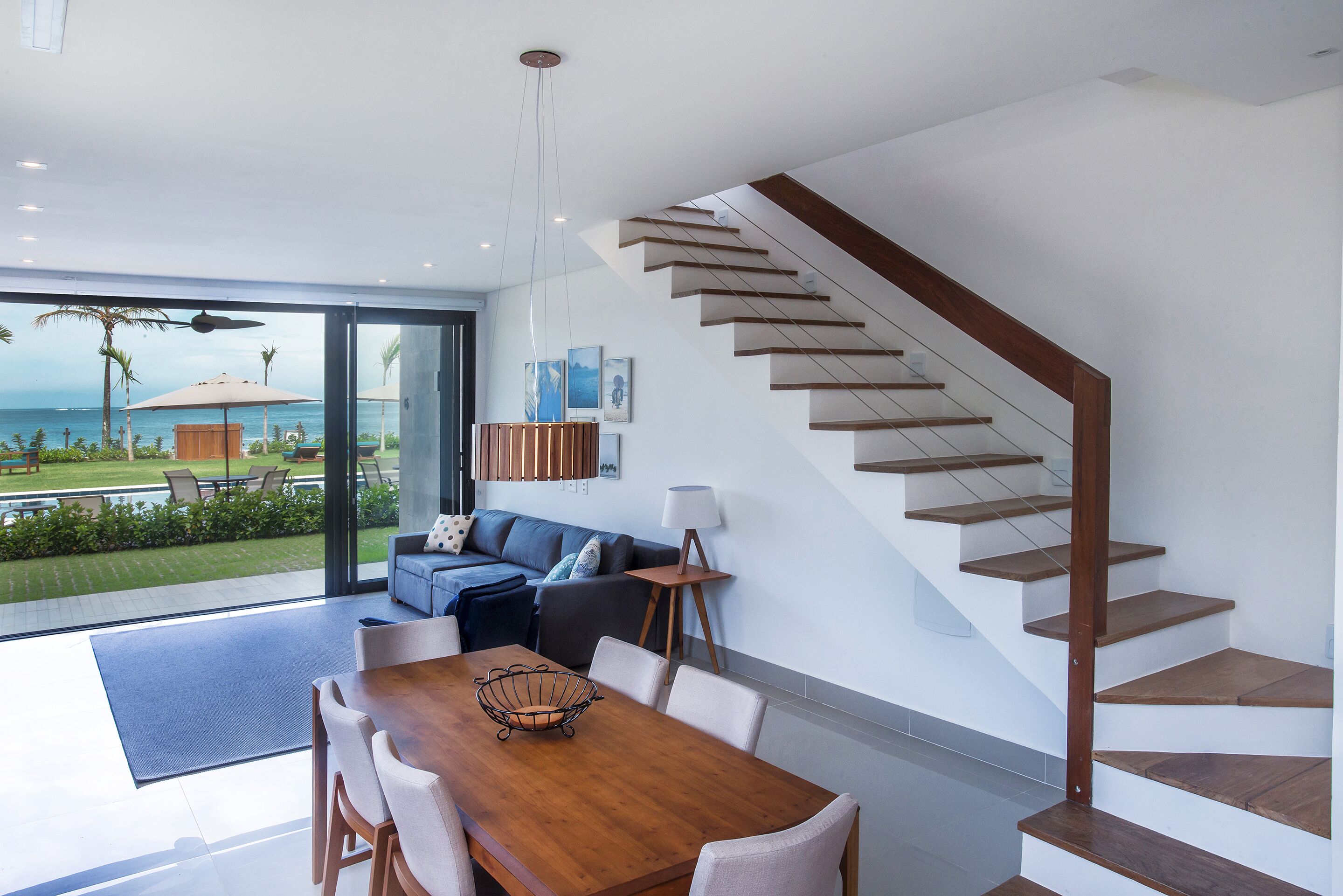 Un intérieur moderne avec une table à manger en bois, un escalier et une vue sur l’extérieur.
