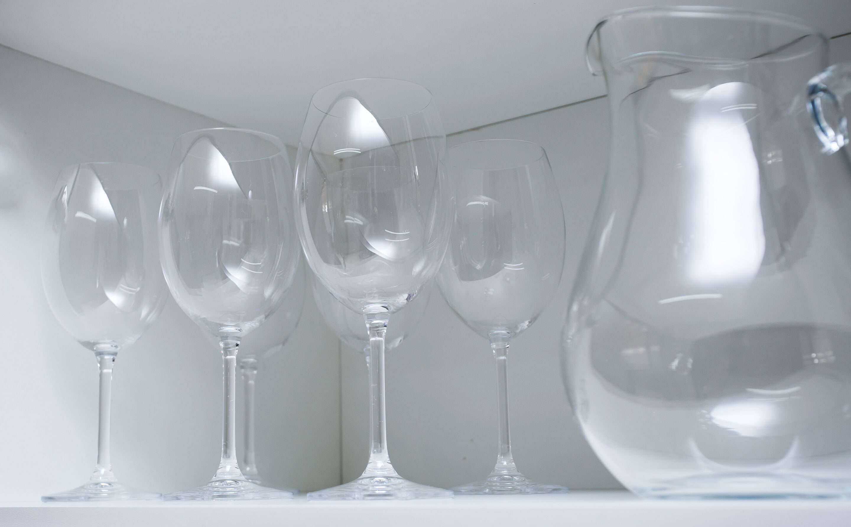 A collection of clear glassware on a shelf, including wine glasses and a pitcher.