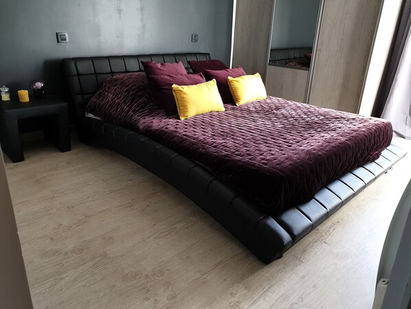 A modern bedroom with a large bed, dark headboard, and a wooden floor. - Grande suite privée avec lit queen size et terrasse privée (Soual)