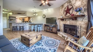 A spacious living area with a stone fireplace, a wooden coffee table, and a ceiling fan. - SS B11 Seele Street River Retreat (New Braunfels)