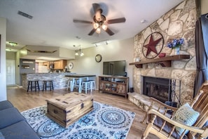 A spacious living area with a stone fireplace, a wooden coffee table, and a ceiling fan.