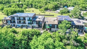 A multi-story residential building with balconies, solar panels, and a green landscape. - SS B11 Seele Street River Retreat (New Braunfels)