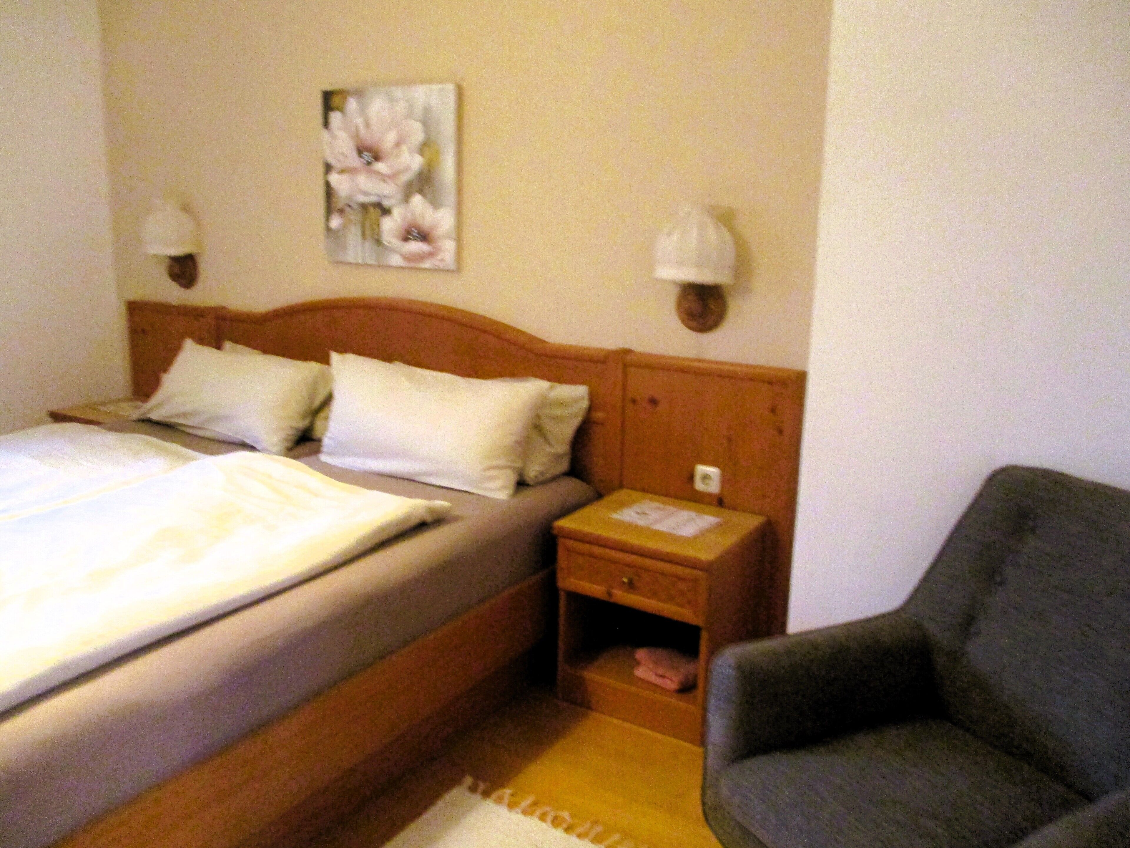A hotel room with a bed, a nightstand, a chair, and a wall-mounted lamp.