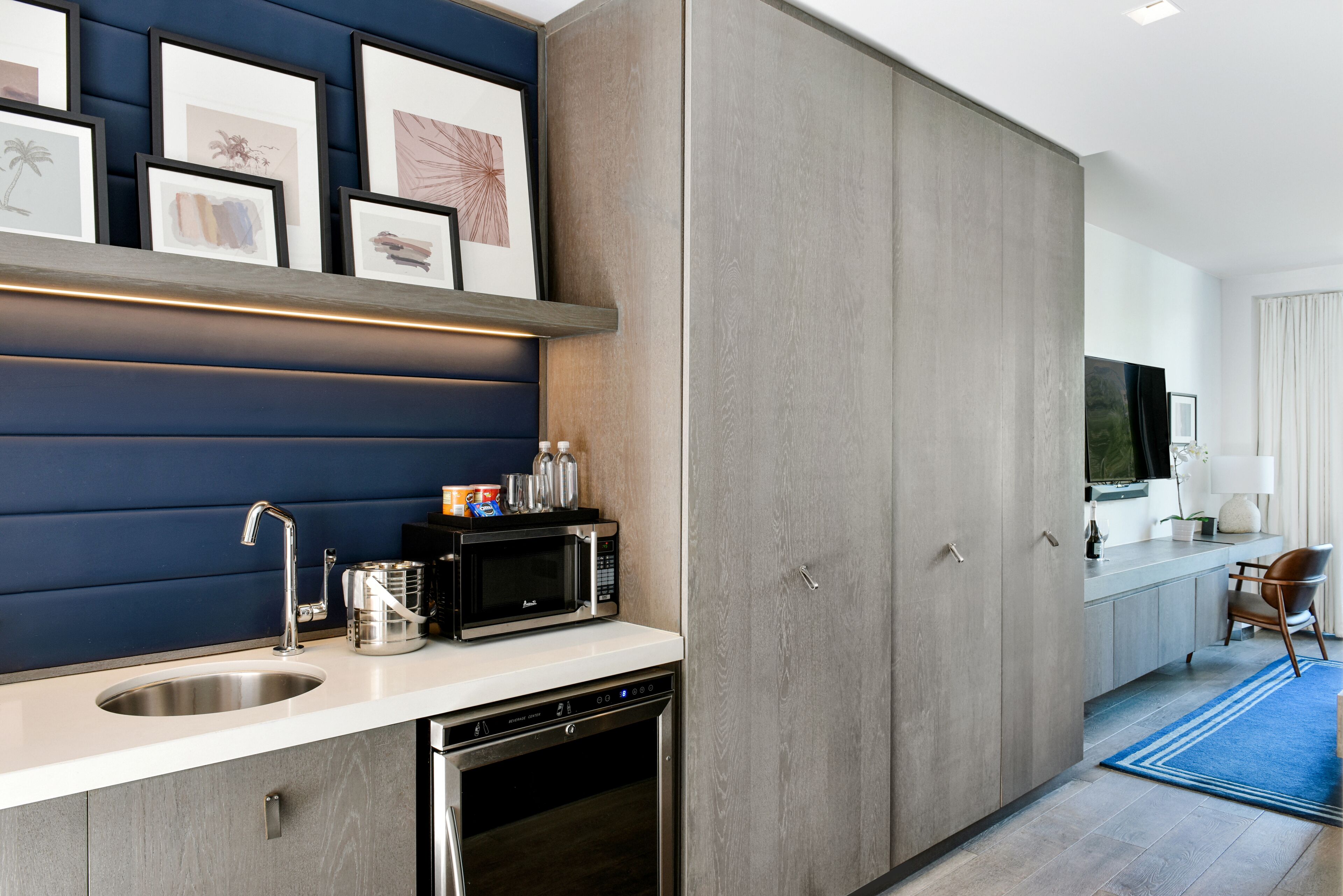 Una cocina moderna con microondas integrado, pileta de acero inoxidable y lavavajillas. Hay cuadros enmarcados en la pared sobre la encimera.