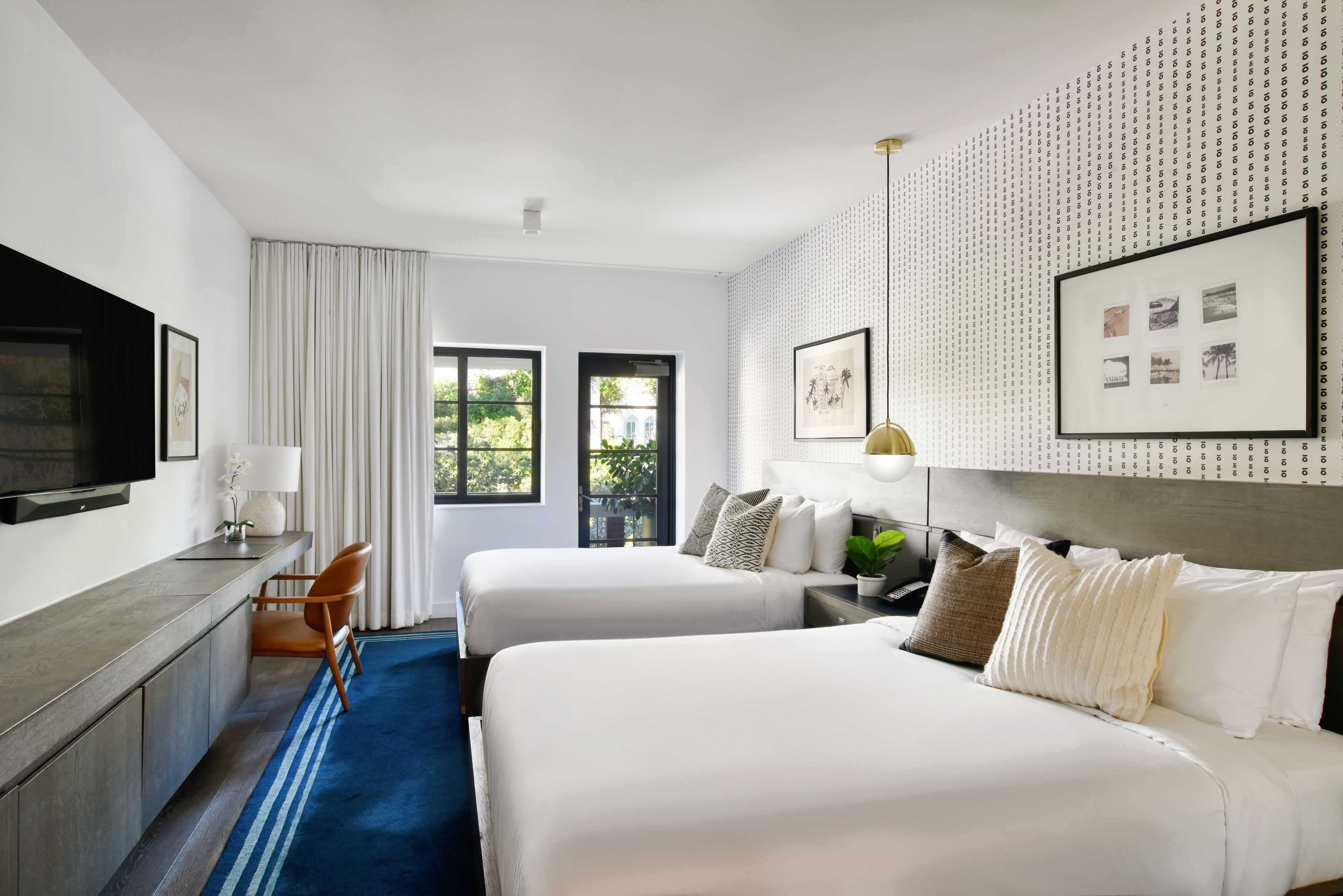 Quarto de hotel com duas camas, uma mesa, uma televisão e uma janela com cortinas.