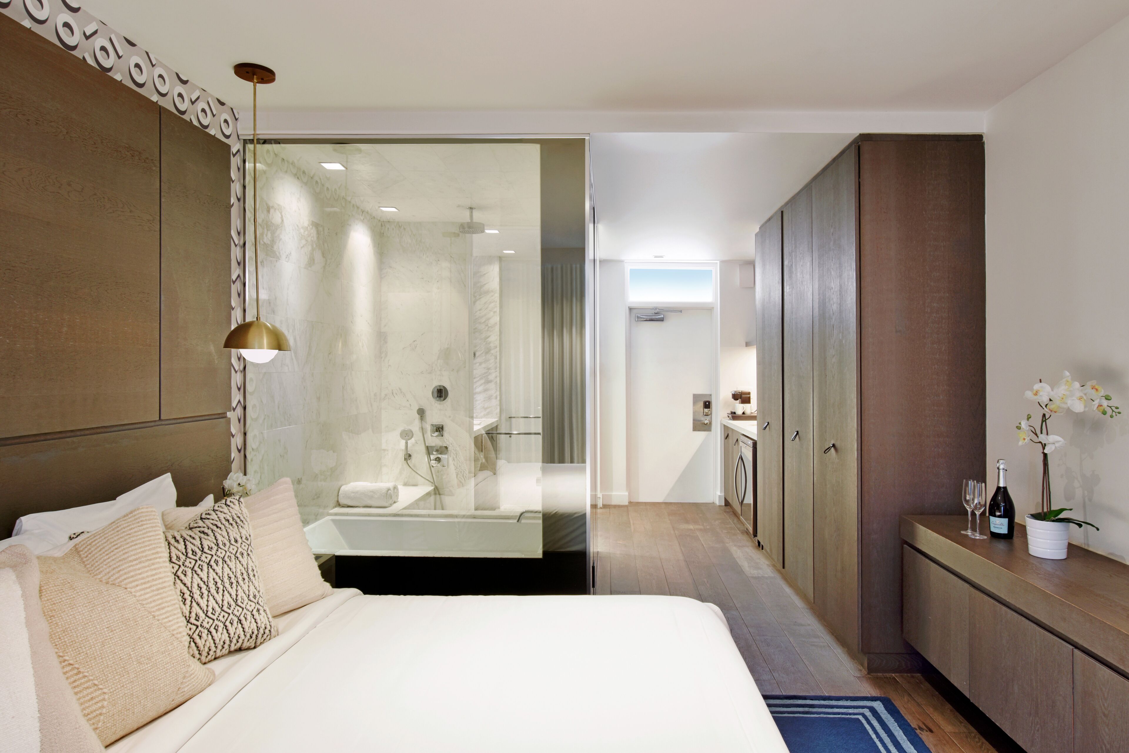 Une chambre d’hôtel moderne avec un grand lit, une douche à parois de verre, une armoire en bois et une petite salle de bain.