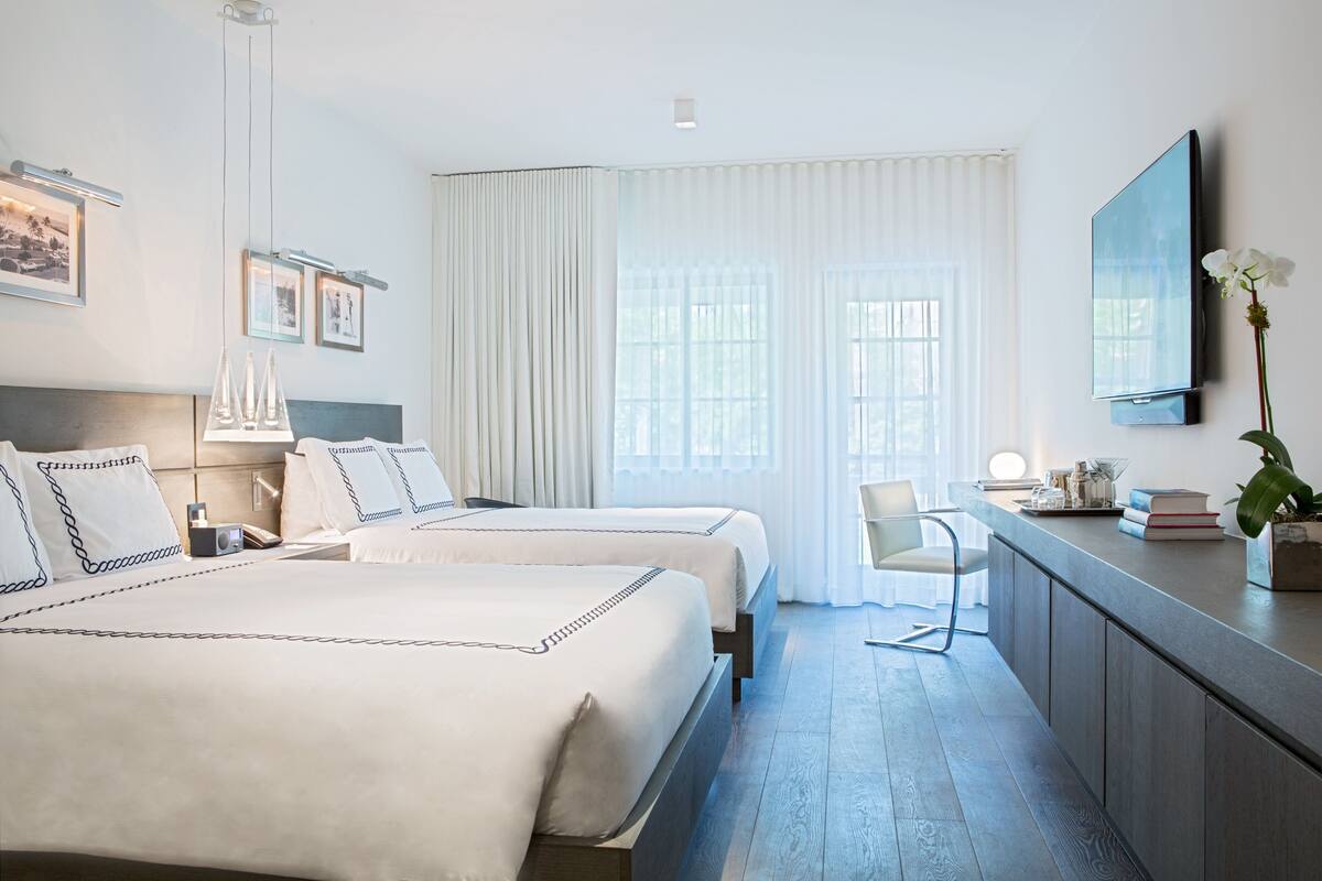 Habitación de hotel con dos camas, un escritorio, una silla, un televisor y una ventana con cortinas.