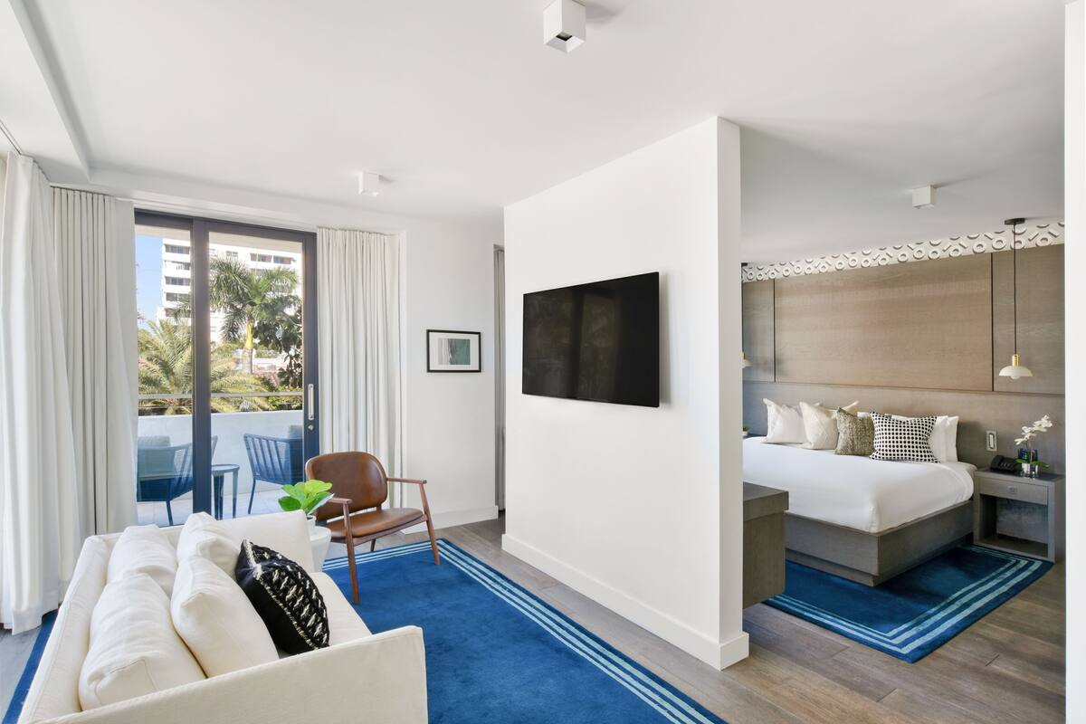 Una habitación de hotel moderna con balcón, cama, zona de estar y televisor.