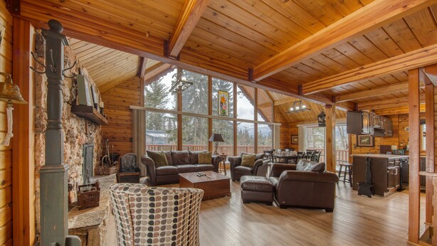 A spacious log cabin with a large living area, wooden floors, and a stone fireplace. - Spring Creek Cabin | 6BR | Hot Tub & Sauna (Fairmont Hot Springs)