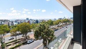 A cityscape view from a balcony with modern buildings, a clear sky, and a tree-lined street. - Designer apartment close to the Waterfront (Cape Town)