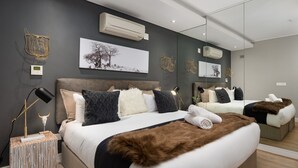 A modern bedroom with a large bed, a bedside table with a lamp, and a wall-mounted air conditioner. - Designer apartment close to the Waterfront (Cape Town)