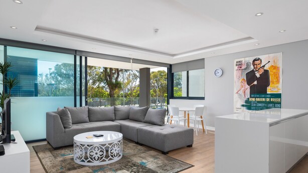 Una sala de estar moderna con un sofá seccional gris, una mesa de centro blanca y un separador de vidrio.