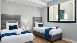 Habitación de hotel con dos camas, un ventanal grande y una mesita de noche con lámpara.