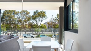 Una habitación moderna con sofá, una mesa y sillas. Hay un ventanal con vistas a la calle y árboles.