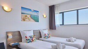 A hotel room with two beds, a painting of a beach, and a window with curtains. - Zenitude Hotel-residences Bordeaux Aeroport Merignac (Merignac)
