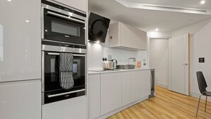 A modern kitchen with built-in appliances, white cabinetry, and a wooden floor. - One Bedroom Apartment at Alie Street in Aldgate London by MySquare (London)