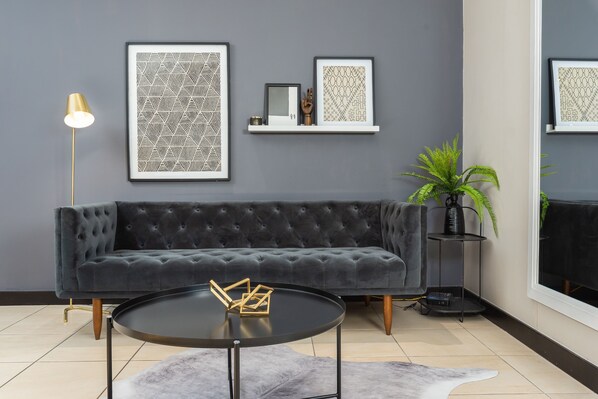 A modern living room with a dark grey sofa, a round black coffee table, and framed artwork on the wall. - Centrally Located Icon Apartment (Cape Town)