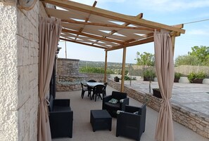 Une terrasse extérieure avec des murs en pierre, une pergola, des meubles en osier et des plantes en pot.