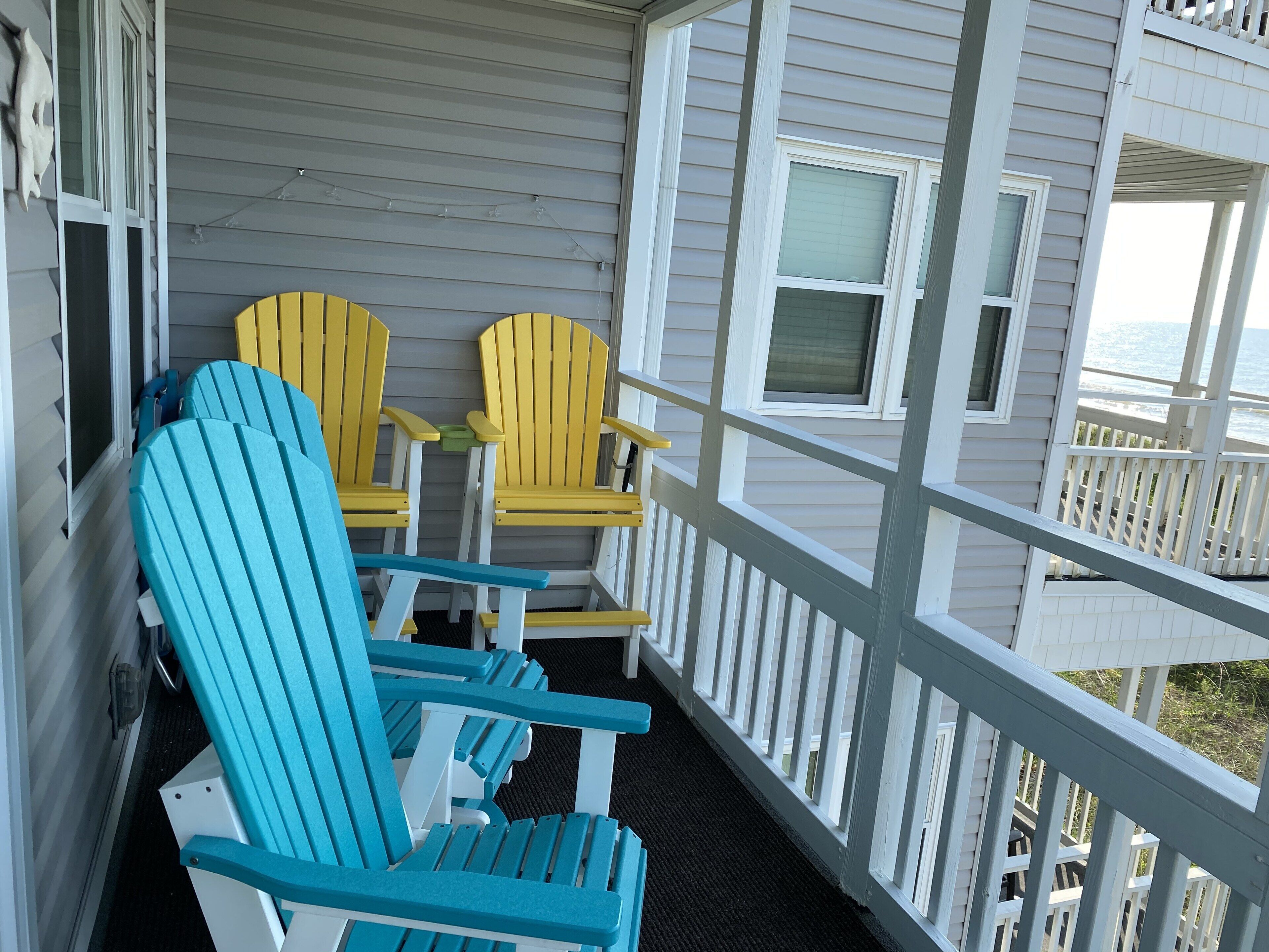 Eine Veranda mit weißen Geländern und blau-gelben Adirondack-Stühlen.