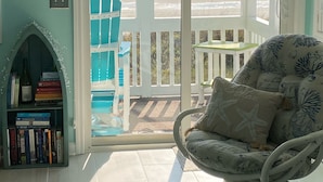 Ein Zimmer mit Blick auf den Strand, ein Bücherregal, ein Sessel mit Kissen in Form eines Seesterns und ein Schild mit der Aufschrift 'Let's Do Sunset'.