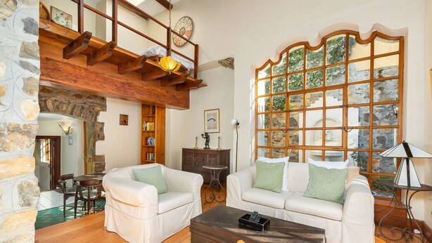A cozy living room with two white sofas, a wooden coffee table, and a stone wall.