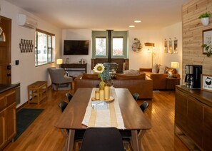 A modern living room with a wooden dining table, sofas, and a TV.