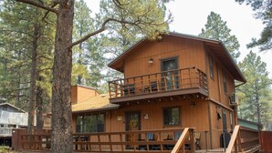 Eine zweistöckige Holzhütte mit Balkon, Veranda und einer Treppe, die zum oberen Stockwerk führt.