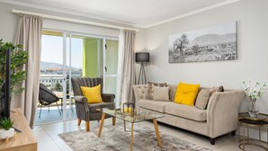 Una sala de estar moderna con un sofá, sillones, una mesa de centro de vidrio y vistas amplias a través de puertas de cristal.