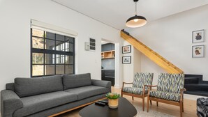 A modern living room with a grey sofa, patterned chairs, a coffee table, and a staircase with wooden beams. - Modern Apartment in De Waterkant l Private Rooftop (Cape Town)