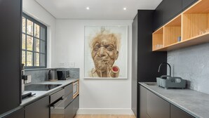 A modern kitchen with dark cabinetry, a wooden countertop, and a large framed artwork on the wall. - Modern Apartment in De Waterkant l Private Rooftop (Cape Town)