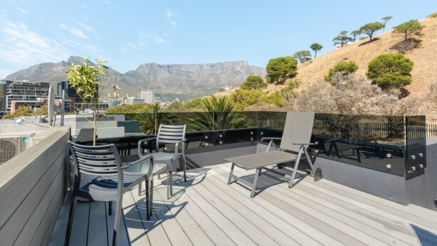 A rooftop terrace with outdoor seating, a view of a mountain range, and a cityscape in the background. - Modern Apartment in De Waterkant l Private Rooftop (Cape Town)