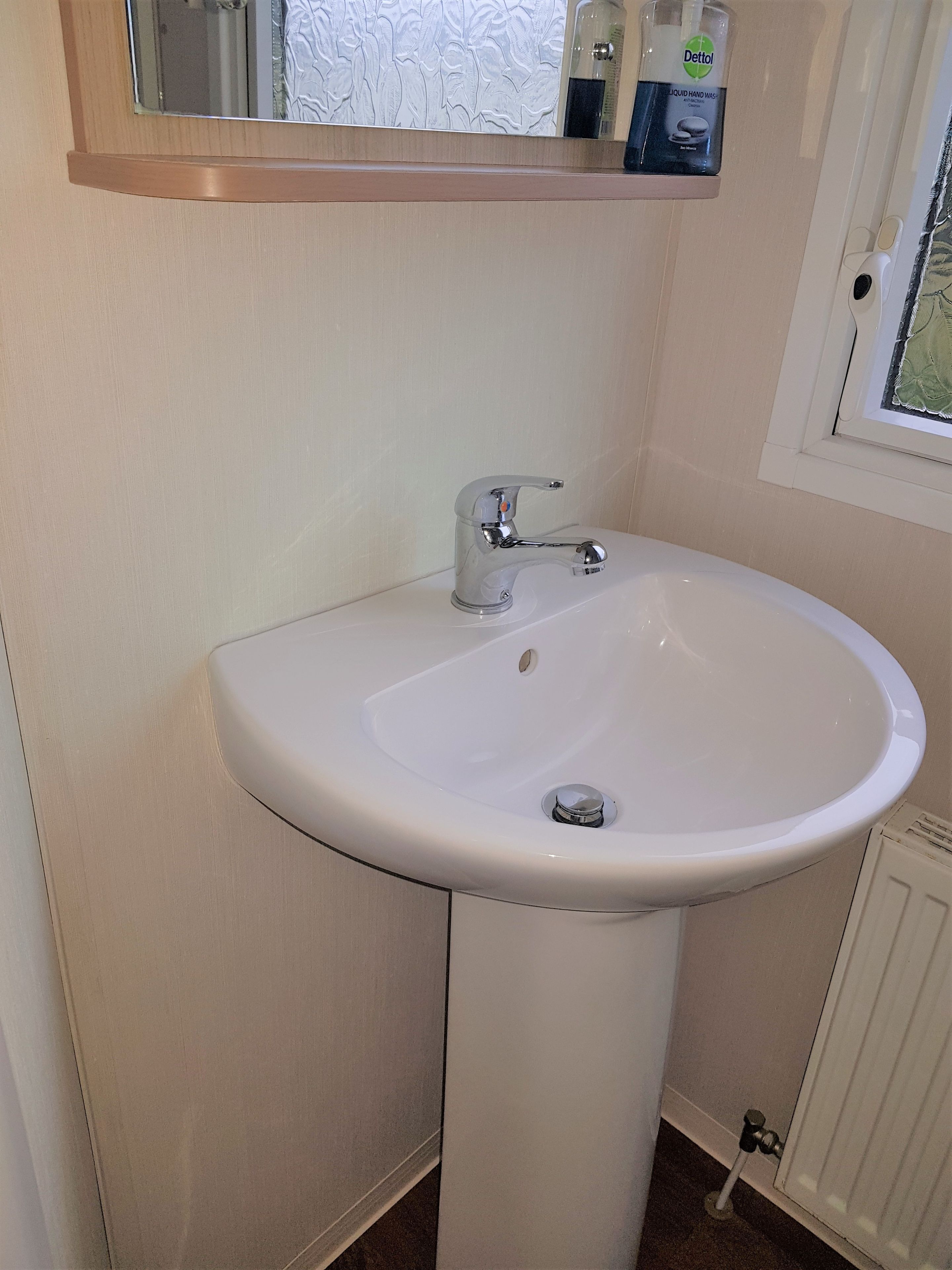 A white bathroom sink with a chrome faucet, a mirror above it, and a window to the right.