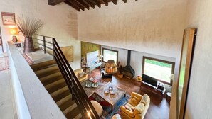 Un amplio salón con techo alto, vigas de madera, chimenea y ventanas grandes.
