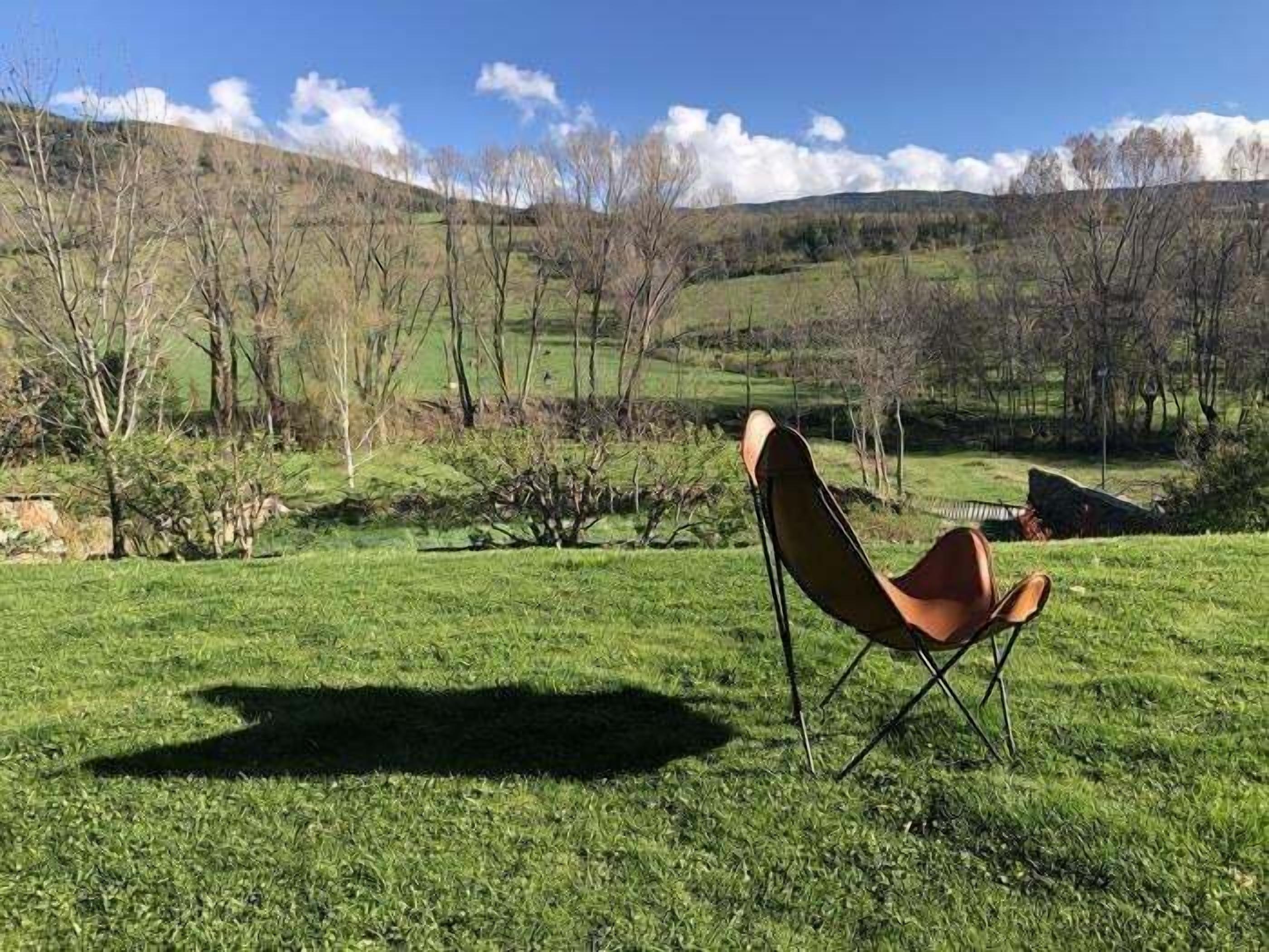 Une chaise posée dans un champ herbeux, à l’air libre, avec une vue sur des collines et des arbres.