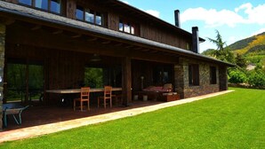 Una casa de madera de dos pisos con un patio cubierto, paredes de piedra y vistas a un paisaje verde.