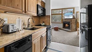 Een moderne keuken met houten kastjes, een stenen openhaard en een groot raam met uitzicht op een besneeerd landschap.