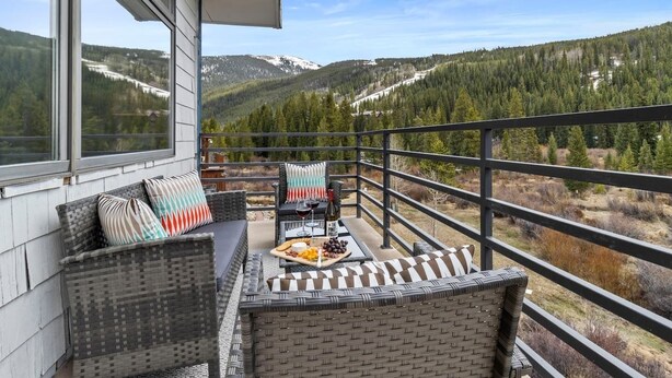 Een balkon met rieten meubilair, een tafel met kaasplank en wijn, en een prachtig uitzicht op de bergen.