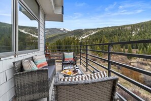 En balkon med fletningsmøbler, et bord med osteanretning og vin, samt en smuk udsigt over bjergene.