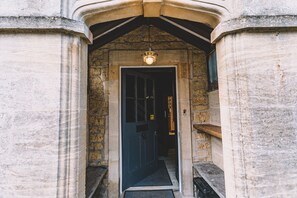 A stone entrance with a dark door, a light fixture above, and a wooden shelf to the right. - Old Bank Rooms (Cheltenham)