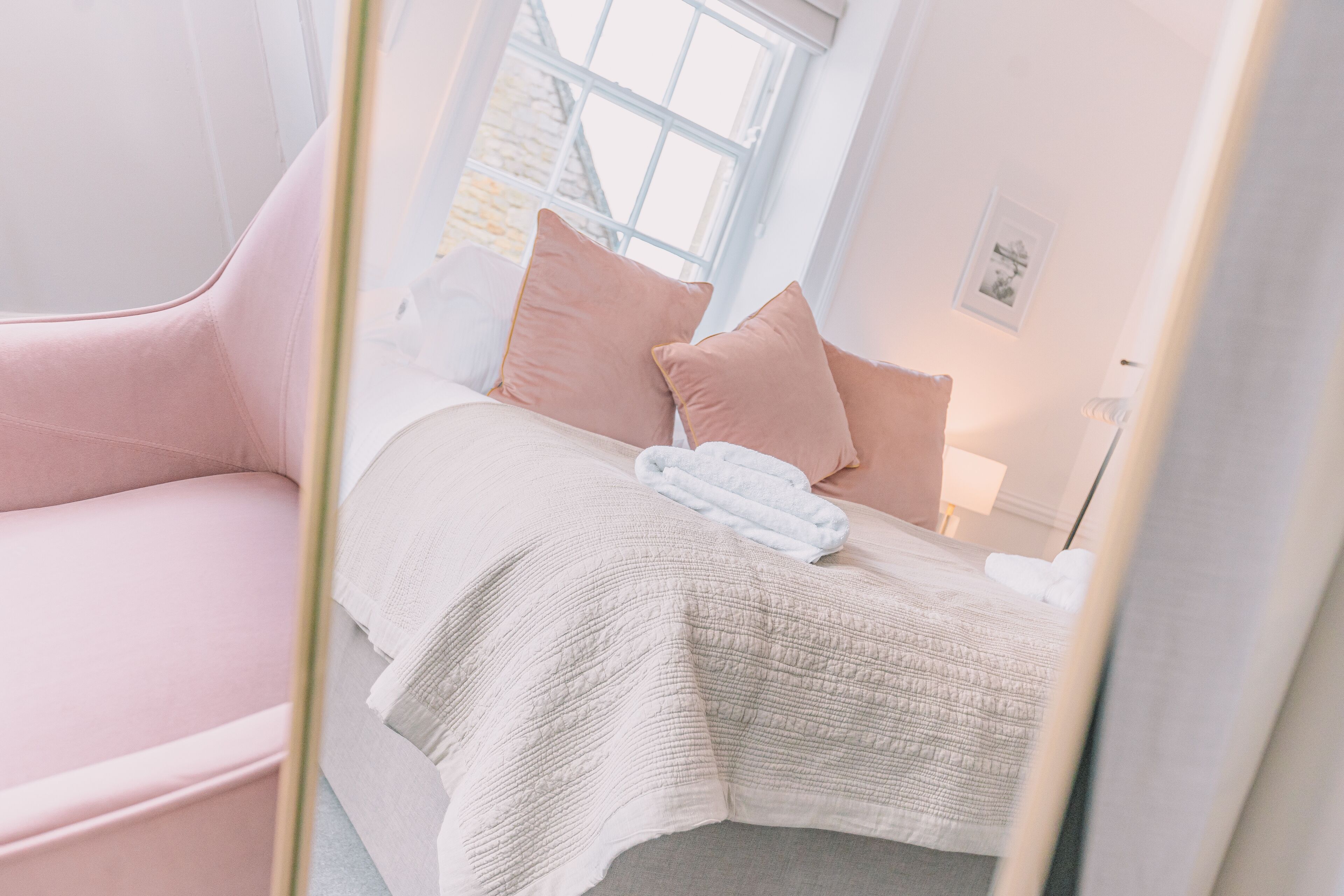 A bedroom with a bed, a pink chair, and a window.