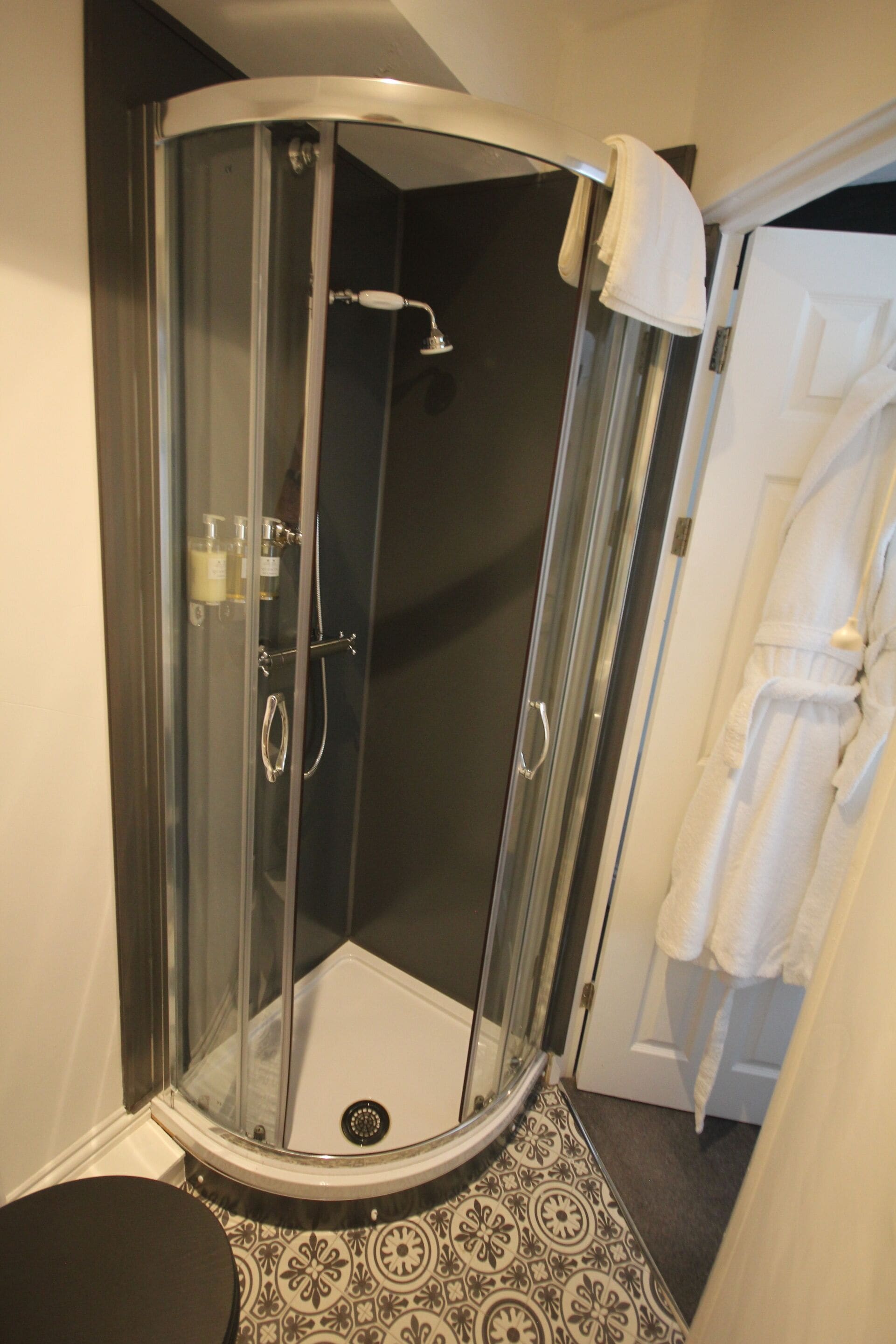 Une douche fermée par des parois de verre, avec une porte blanche, un porte-serviettes et un carrelage à motifs.