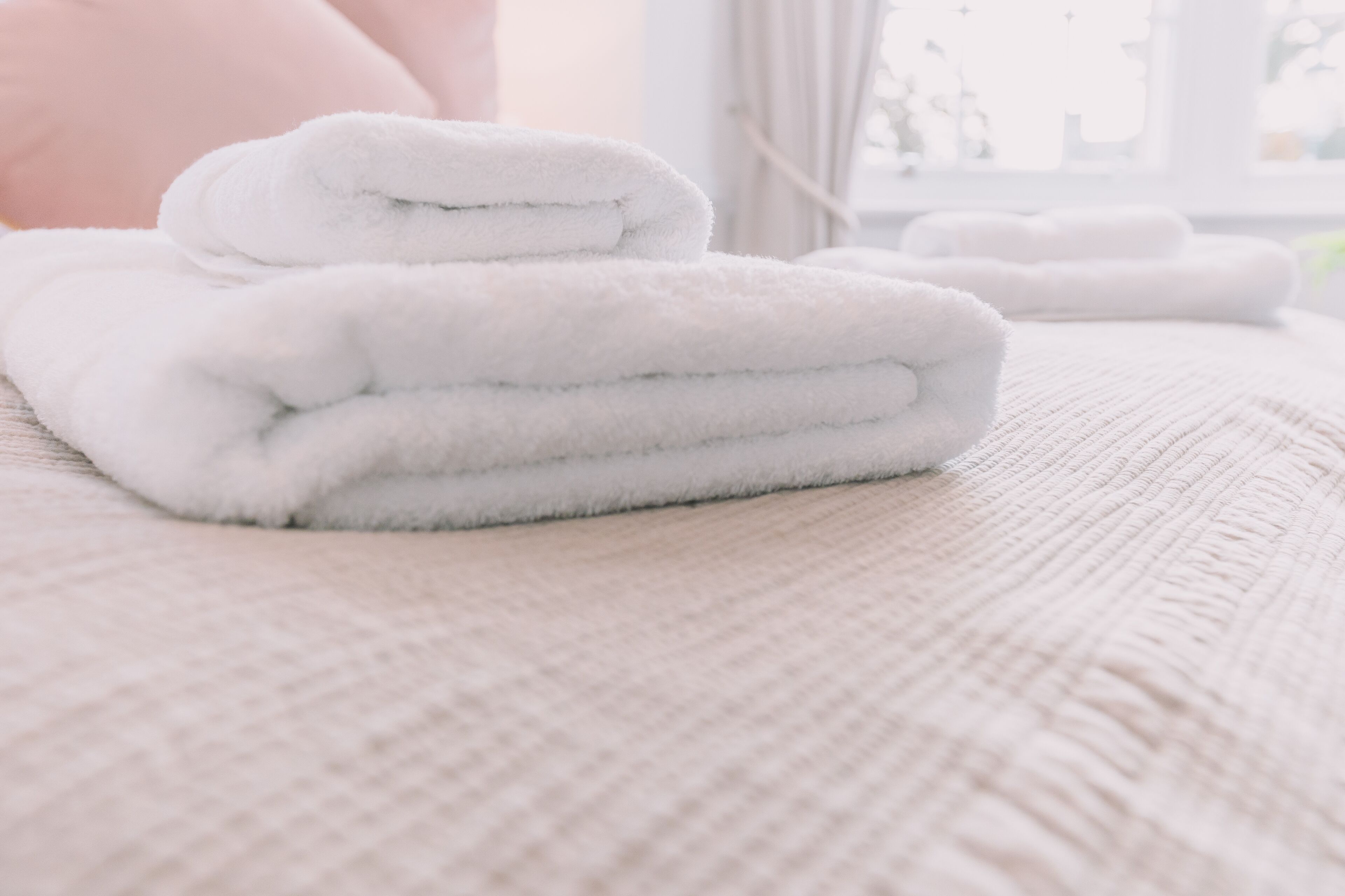 A neatly folded stack of white towels on a textured beige bedspread.