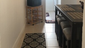 A narrow hallway with a dining area featuring a dark wooden table and bar stools. A microwave is on a small wooden cart, and there are decorative wall art pieces. - PRIME DELRAY BEACH, CHARMING 2 BEDROOM COTTAGE, PETS WELCOME  (Delray Beach)