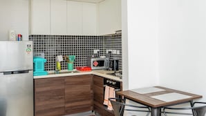 Een kleine keuken met een koelkast, magnetron, broodrooster en een eettafel met stoelen.
